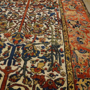 Multicolored traditional rug featuring an ivory field with dense botanical motifs and a rust-red border on wood planks.