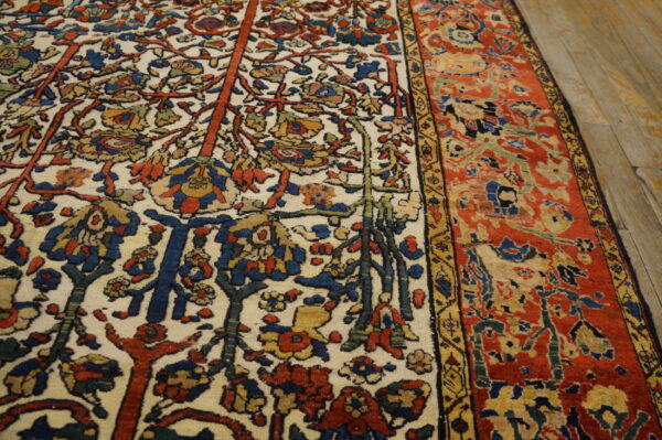 Multicolored traditional rug featuring an ivory field with dense botanical motifs and a rust-red border on wood planks.