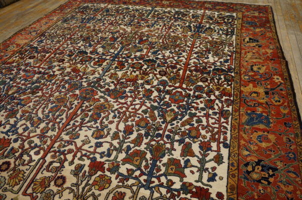 Detailed rug with a cream field, multicolored botanical patterns, and a wide red border, lying on wood floors.