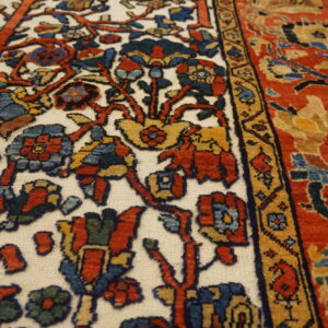 Detailed view of a traditional rug with contrasting red and ivory panels and complex floral floral designs.