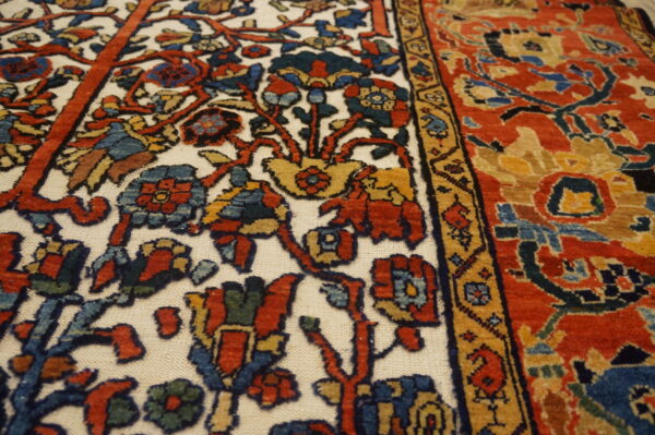 Detailed view of a traditional rug with contrasting red and ivory panels and complex floral floral designs.