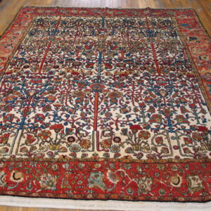 Detailed floral and tree pattern rug with red borders and an ivory field on wooden flooring.