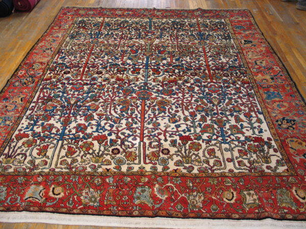 Detailed floral and tree pattern rug with red borders and an ivory field on wooden flooring.