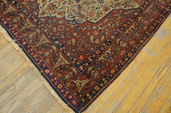 Low-pile oriental rug corner featuring red and blue floral borders on distressed yellow plank flooring.