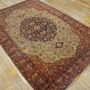 Low-pile floral rug featuring navy, rust, and beige colors on a heavily worn light wooden floor.
