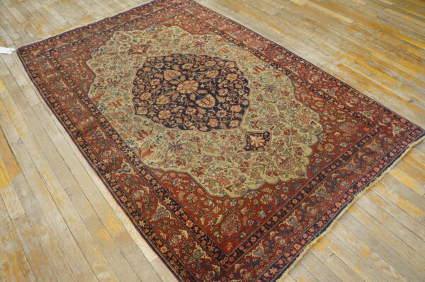 Low-pile floral rug featuring navy, rust, and beige colors on a heavily worn light wooden floor.