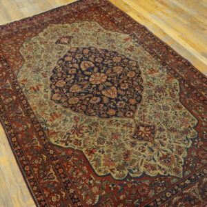 Ornate floral rug with a navy center medallion, gold field, and deep red border on wood plank flooring.