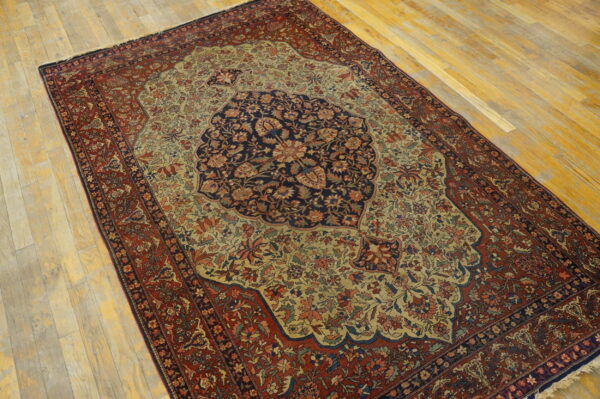 Ornate floral rug with a navy center medallion, gold field, and deep red border on wood plank flooring.