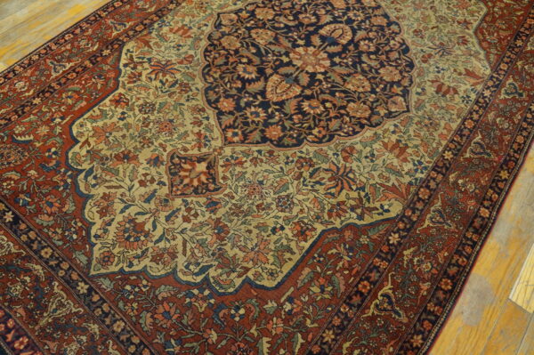 Traditional rug featuring a navy medallion, beige floral field, and rust borders on wood planks.