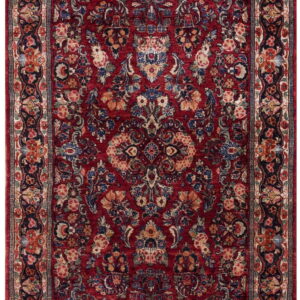 A high-pile, rectangular rug features a dense floral design in deep red, navy blue, cream, and gold tones.