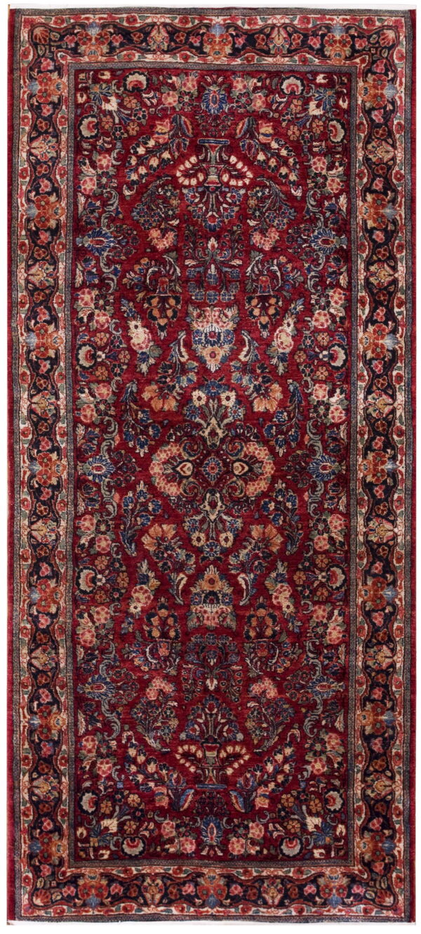 A high-pile, rectangular rug features a dense floral design in deep red, navy blue, cream, and gold tones.