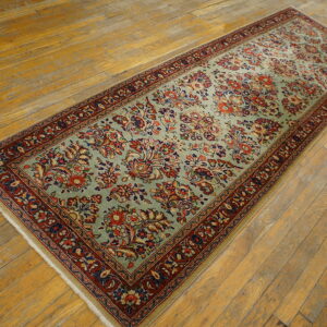 Light green floral runner rug with a deep red border, laid diagonally across distressed wood planks.