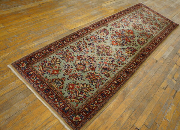 Light green floral runner rug with a deep red border, laid diagonally across distressed wood planks.