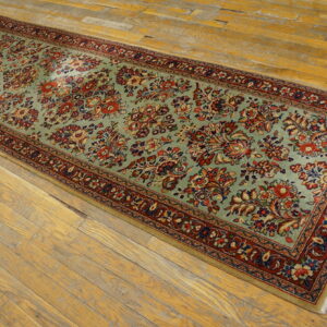 Long runner rug with a light blue-green field and multi-colored floral pattern lies on distressed wood flooring.