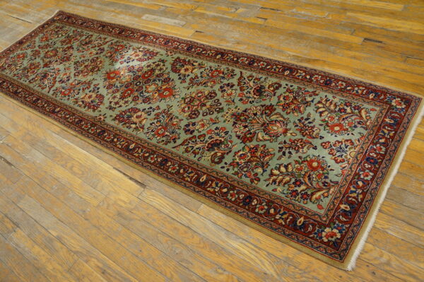 Long runner rug with a light blue-green field and multi-colored floral pattern lies on distressed wood flooring.