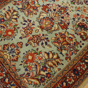 Pale sage green rug featuring dense red and blue traditional floral patterns and a wide red border on wood floor.