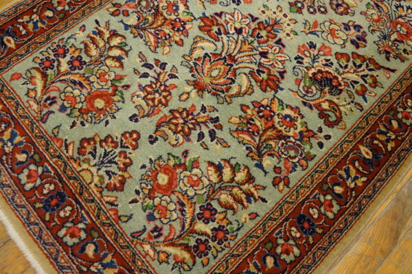 Pale sage green rug featuring dense red and blue traditional floral patterns and a wide red border on wood floor.