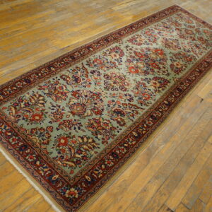 A long blue-green runner rug with red and navy floral patterns rests on distressed hardwood floors.
