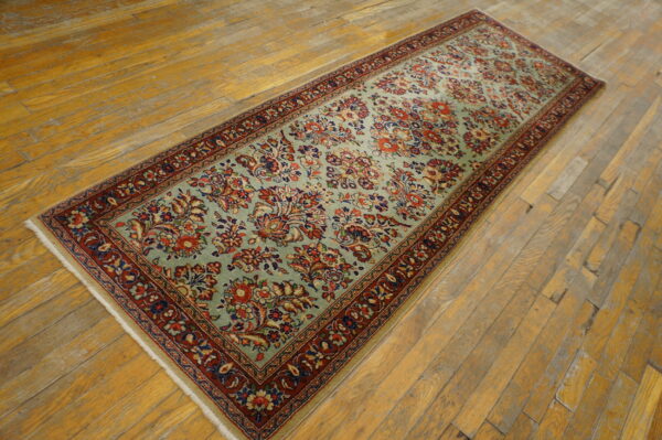 A long blue-green runner rug with red and navy floral patterns rests on distressed hardwood floors.