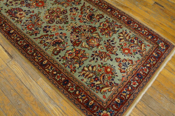 Seafoam green rug with a dense traditional red and blue floral pattern on worn yellow wood planks.