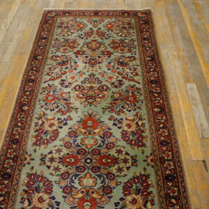 A light blue-green traditional runner rug with detailed red and navy florals covers distressed wooden planks.
