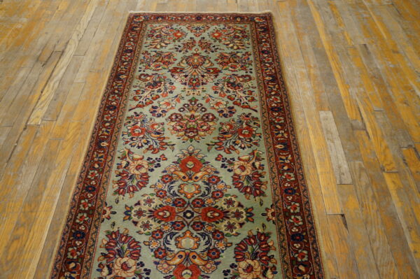 A light blue-green traditional runner rug with detailed red and navy florals covers distressed wooden planks.
