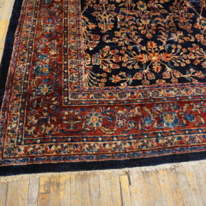 Navy and red traditional rug featuring intricate floral patterns and fringe on light wood plank flooring.