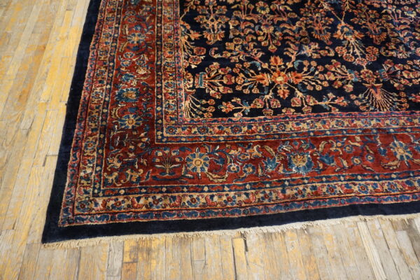 Navy and red traditional rug featuring intricate floral patterns and fringe on light wood plank flooring.