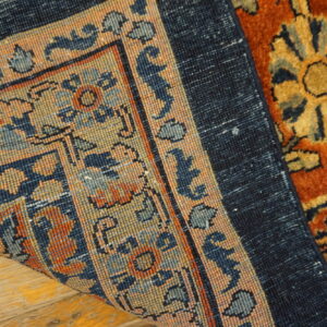 Folded rug corner displays a flat navy blue backing and the front's dense rust and gold floral pattern.
