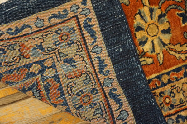 Folded rug corner displays a flat navy blue backing and the front's dense rust and gold floral pattern.