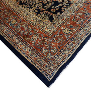 Corner view of a traditional rug featuring a dark navy center and an intricate rust and beige floral border.