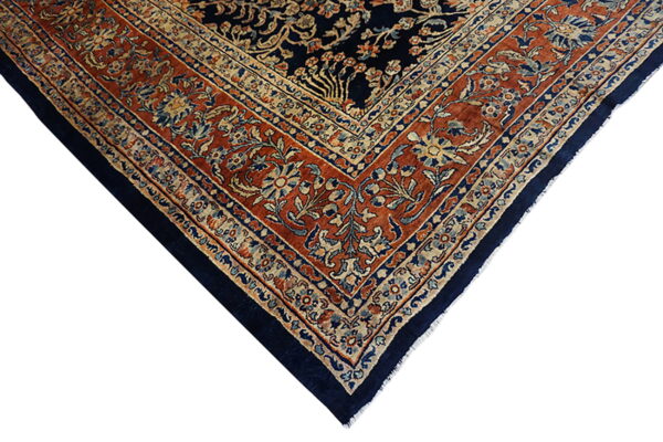 Corner view of a traditional rug featuring a dark navy center and an intricate rust and beige floral border.