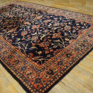 Large navy rug features a dense floral pattern and rust border, lying on light wood planks.