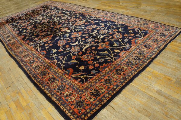 Large navy rug features a dense floral pattern and rust border, lying on light wood planks.