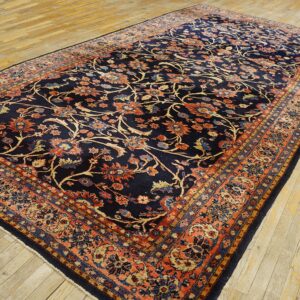 Ornate navy blue rug featuring rust-colored floral motifs and a detailed border on light wood flooring.