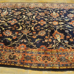 Navy floral rug featuring rust, peach, and blue accents, bordered by coordinating intricate bands on wood floor.