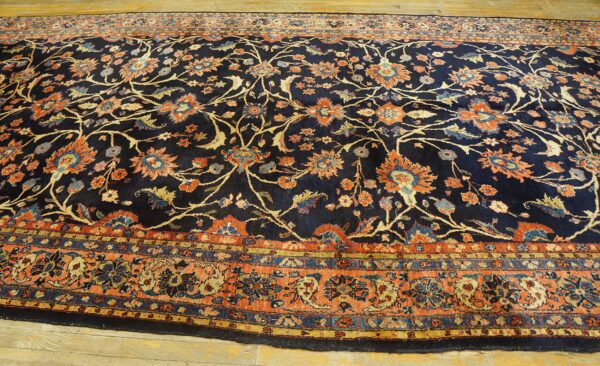 Navy floral rug featuring rust, peach, and blue accents, bordered by coordinating intricate bands on wood floor.