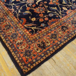 High pile navy and rust floral rug displayed on distressed light wood plank flooring.