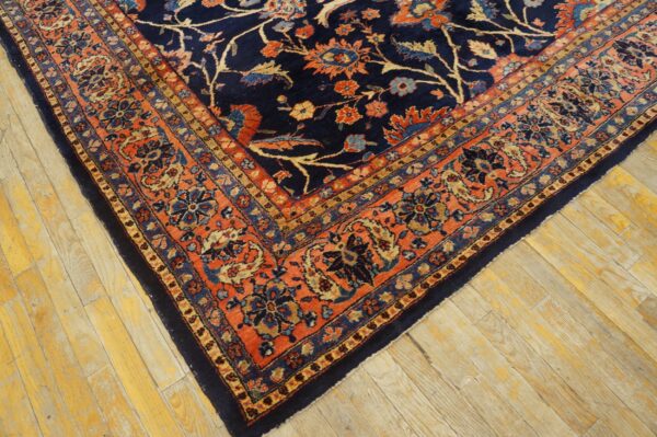 High pile navy and rust floral rug displayed on distressed light wood plank flooring.