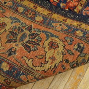 Tightly woven rug in rust, navy, and gold intricate patterns resting on light wood flooring.
