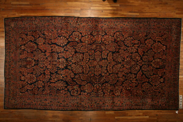 Large black and rust rug featuring an intricate floral design, displayed flat on light wood planks.