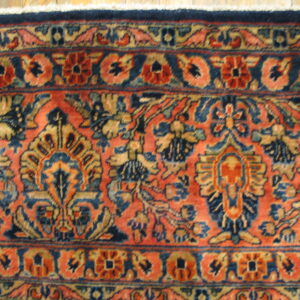 Intricate salmon and navy rug with dense floral motifs rests on light wood flooring.