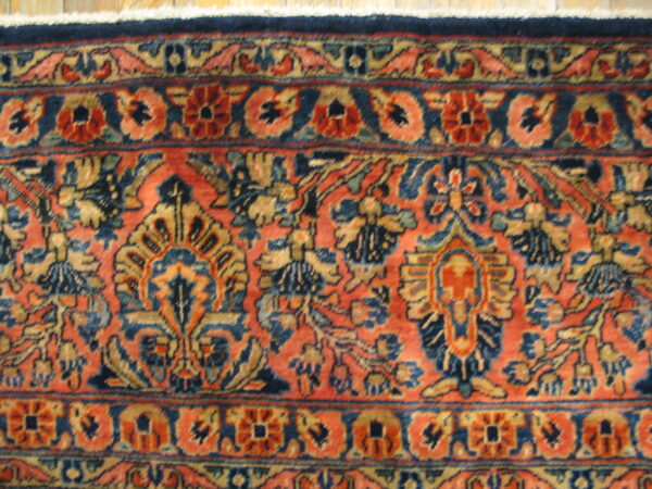 Intricate salmon and navy rug with dense floral motifs rests on light wood flooring.