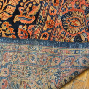 Close-up of a navy and orange high-pile rug with the woven backing visible on light wood flooring.