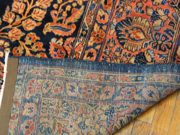 Close-up of a navy and orange high-pile rug with the woven backing visible on light wood flooring.