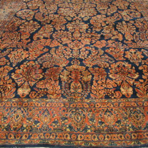 Intricate rust and gold floral patterns cover a dark navy rug laid over a wooden floor.