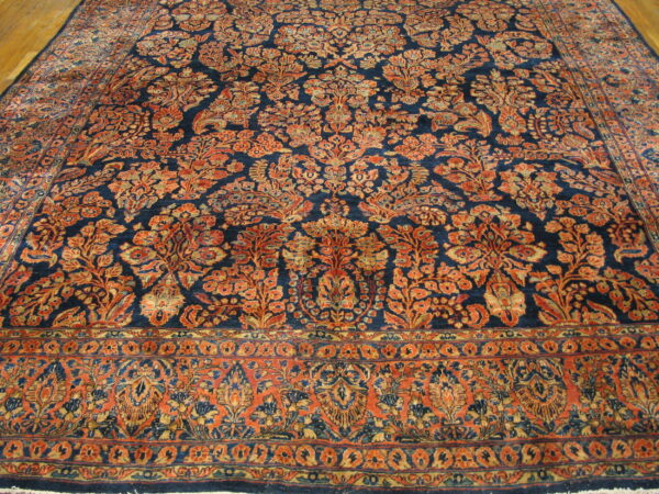 Intricate rust and gold floral patterns cover a dark navy rug laid over a wooden floor.