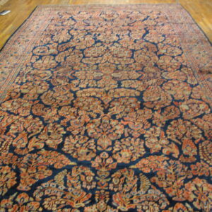 Long area rug with dense orange and tan floral motifs against a navy blue field on wood flooring.