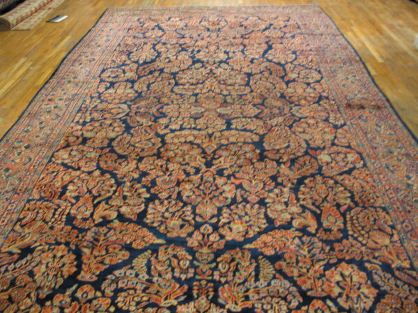 Long area rug with dense orange and tan floral motifs against a navy blue field on wood flooring.