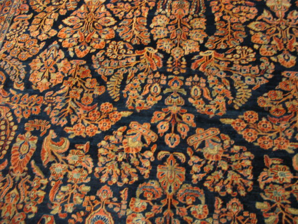 High-pile rug featuring dense orange and gold floral motifs against a navy blue background.